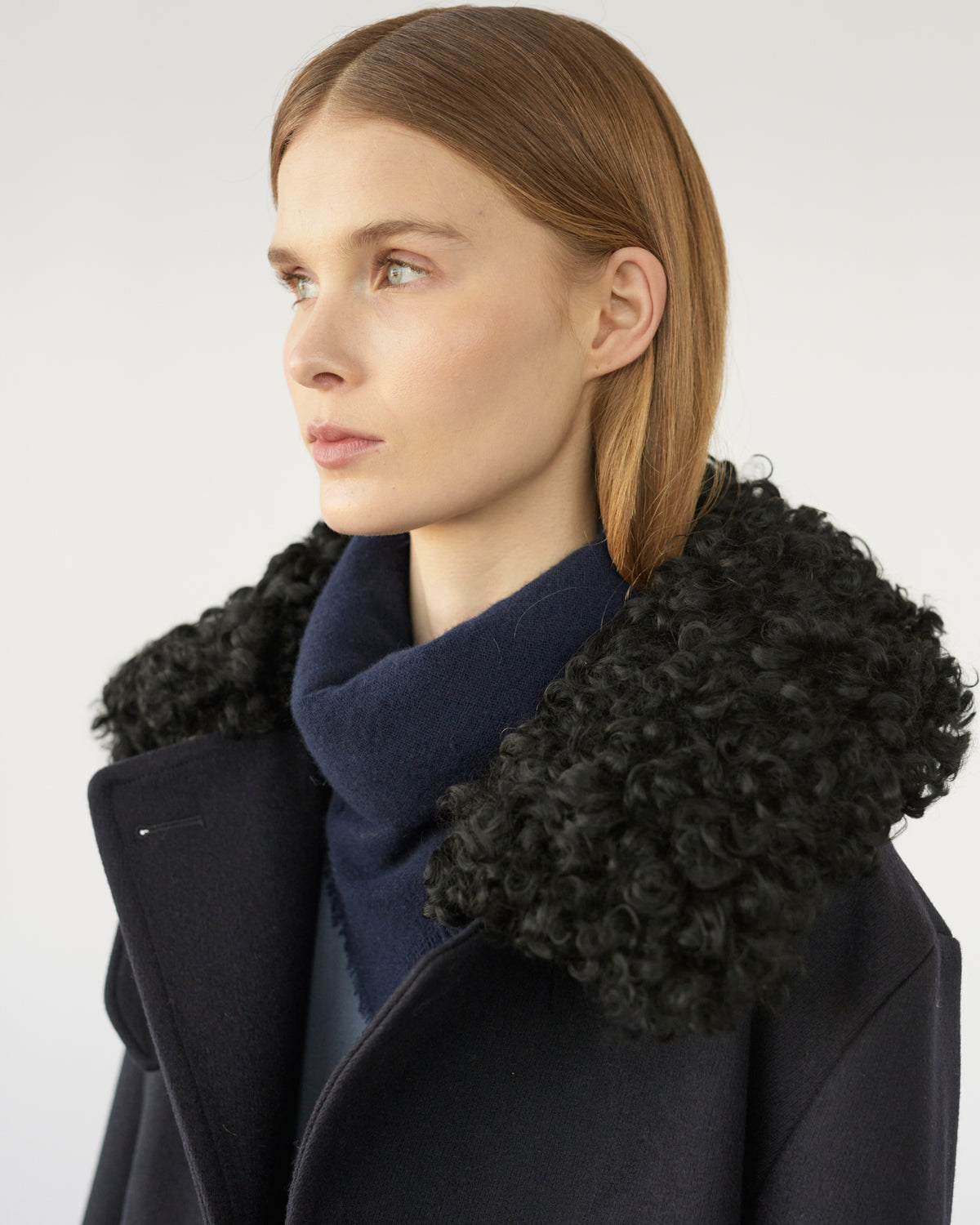 Model wearing a navy coat with a black sheep collar against a white background