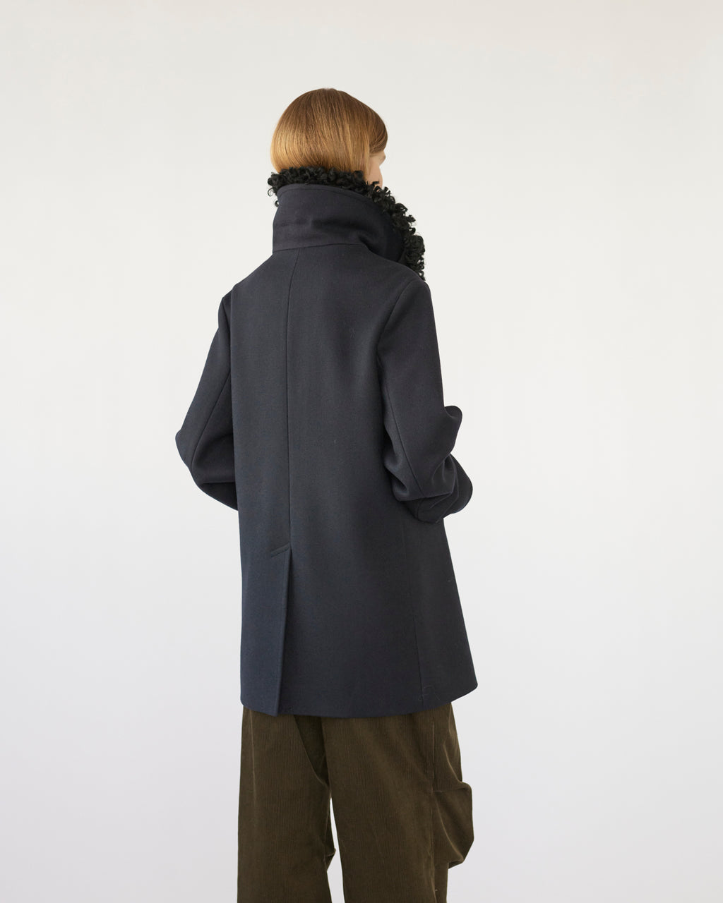 Model wearing a navy Peacoat with a black sheep collar on a white background back view