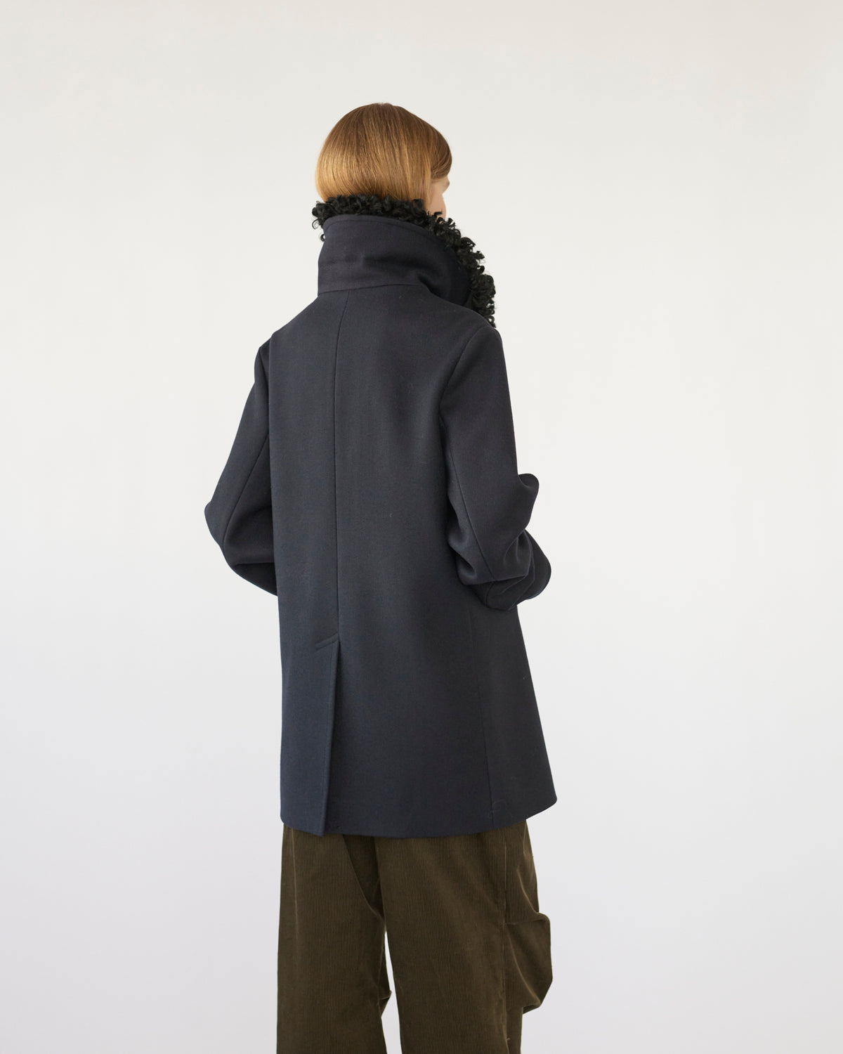 Model wearing a navy Peacoat with a black sheep collar on a white background back view