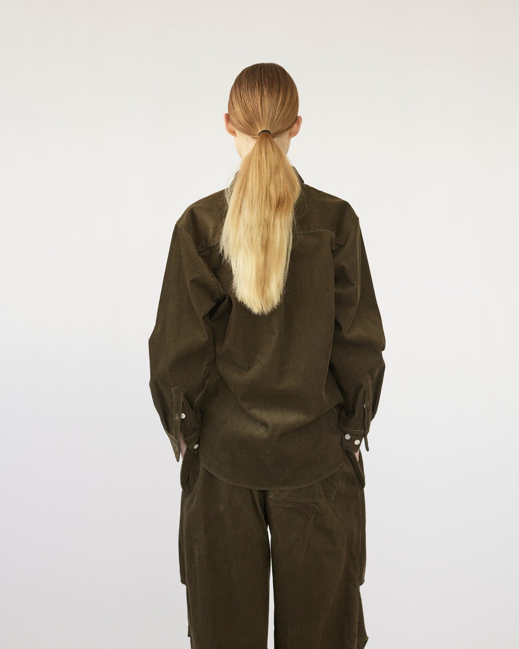 Model wearing a olive shirt and pants with a plain white background. Back view 