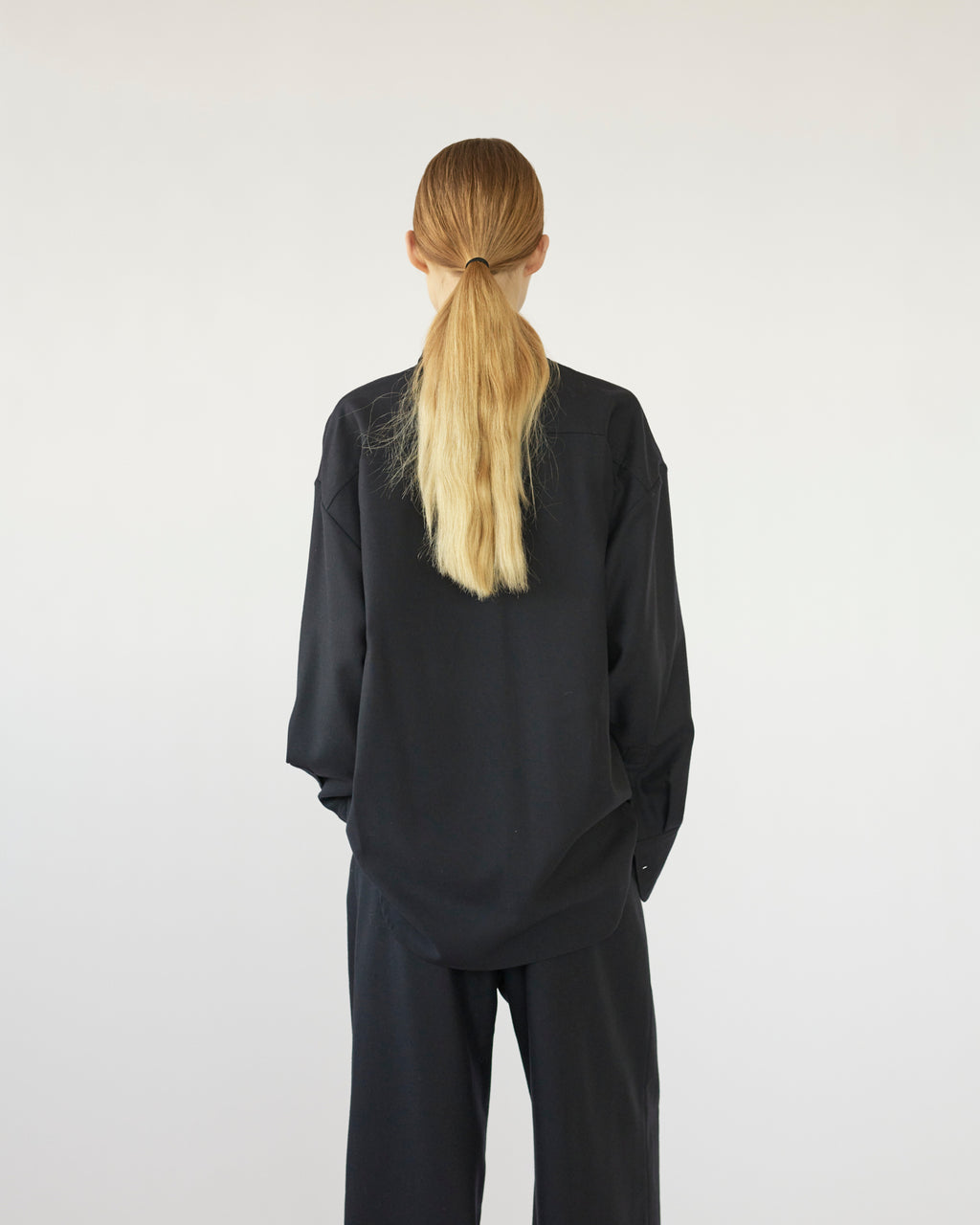 Model wearing a navy outfit with a ponytail on a white background. Back side
