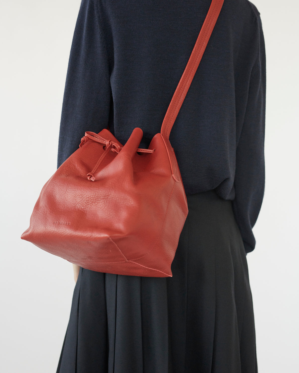 Person wearing a red bucket leather bag over one shoulder on a plain background