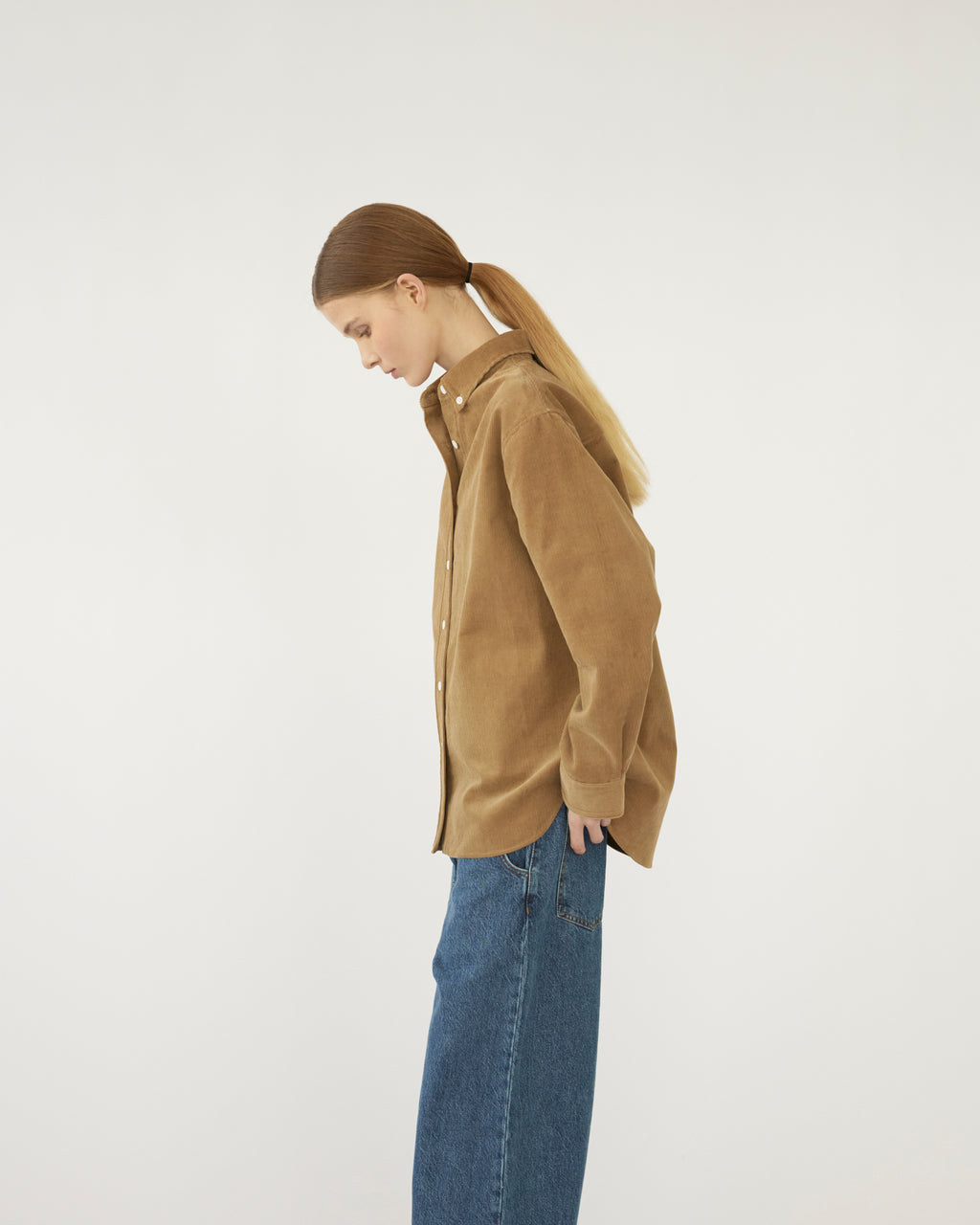 Model wearing a brown shirt and blue jeans on a white background. Side view