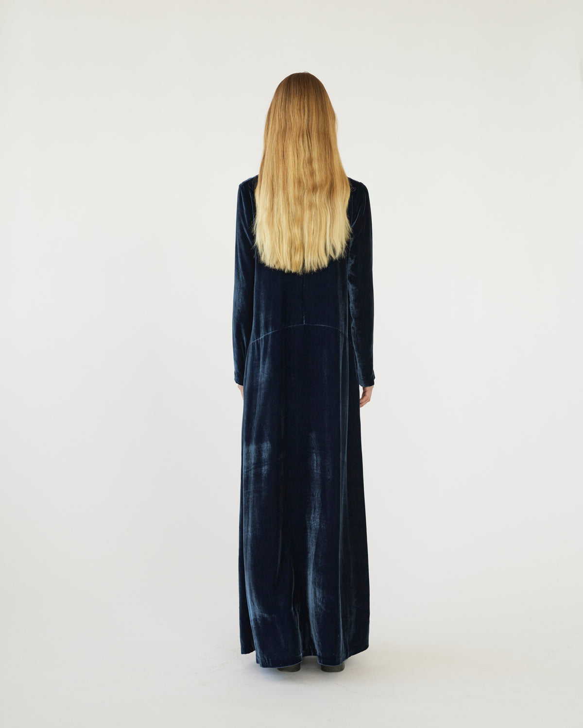 Model wearing a long navy velvet dress against a white background. Back view