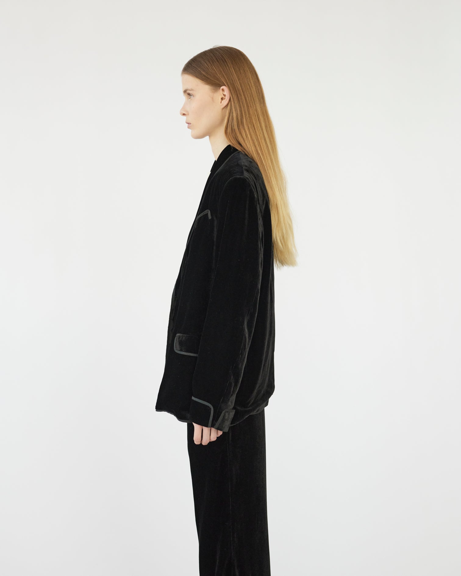 Model wearing a silk velvet black suit on a white background. Side view 