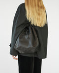 Person wearing a black drawstring bag over shoulder on a white background