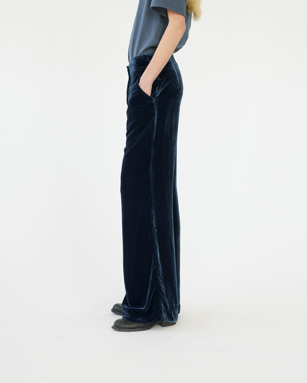 Model wearing dark blue velvet pants on a white background. Side view