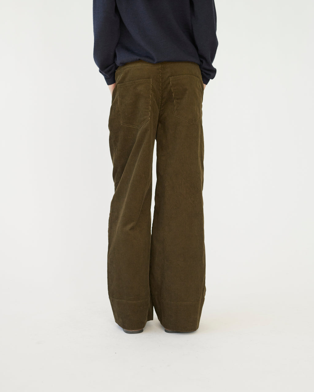 The model is wearing a pair of olive -colored corduroy trousers against a white background back view.