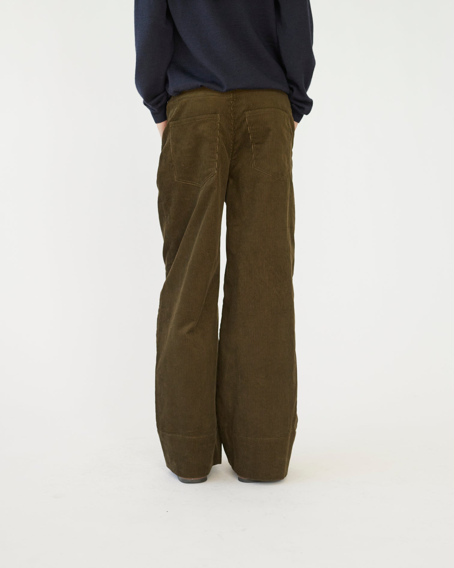The model is wearing a pair of olive -colored corduroy trousers against a white background back view.