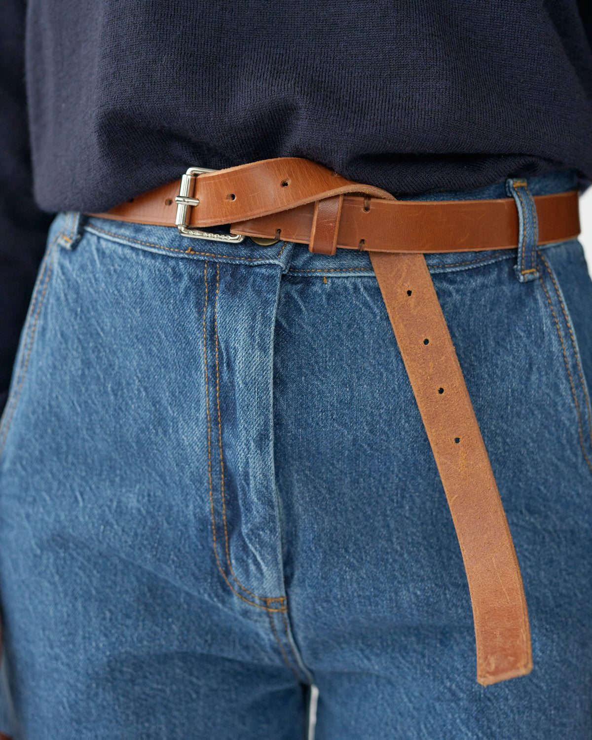 Person wearing blue jeans with a brown leather belt