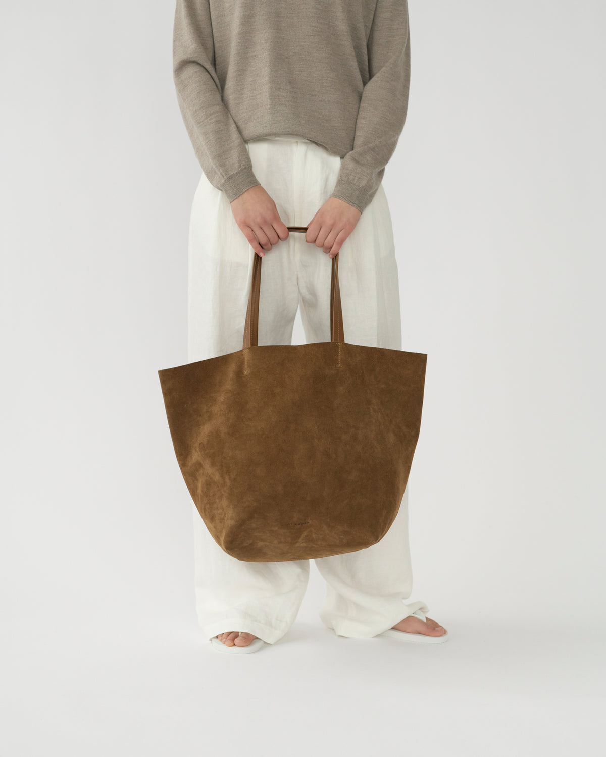 Model holding a brown suede tote bag against a plain background. Front view