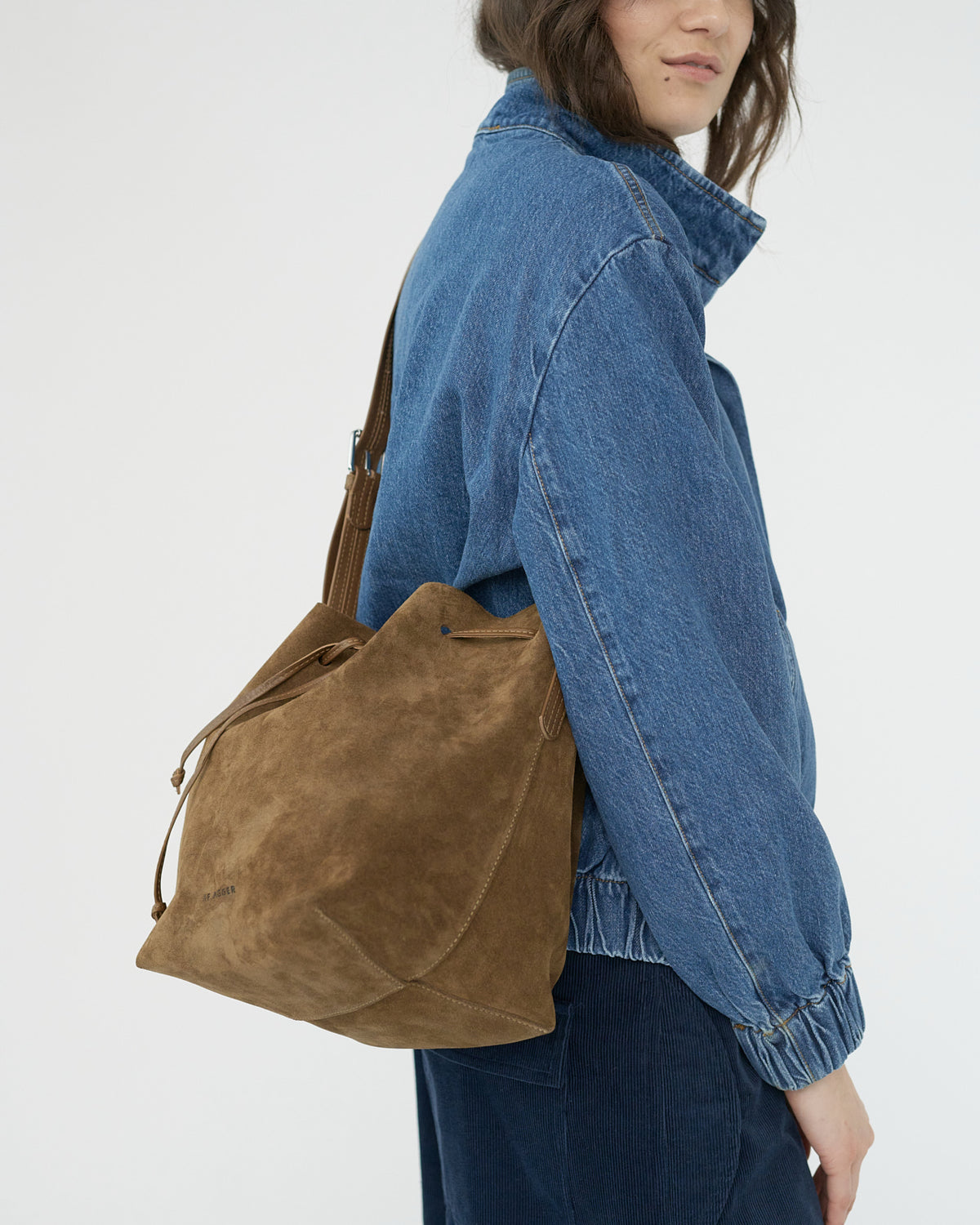 Model wearing a blue denim jacket with a brown suede bag over one shoulder on a white background