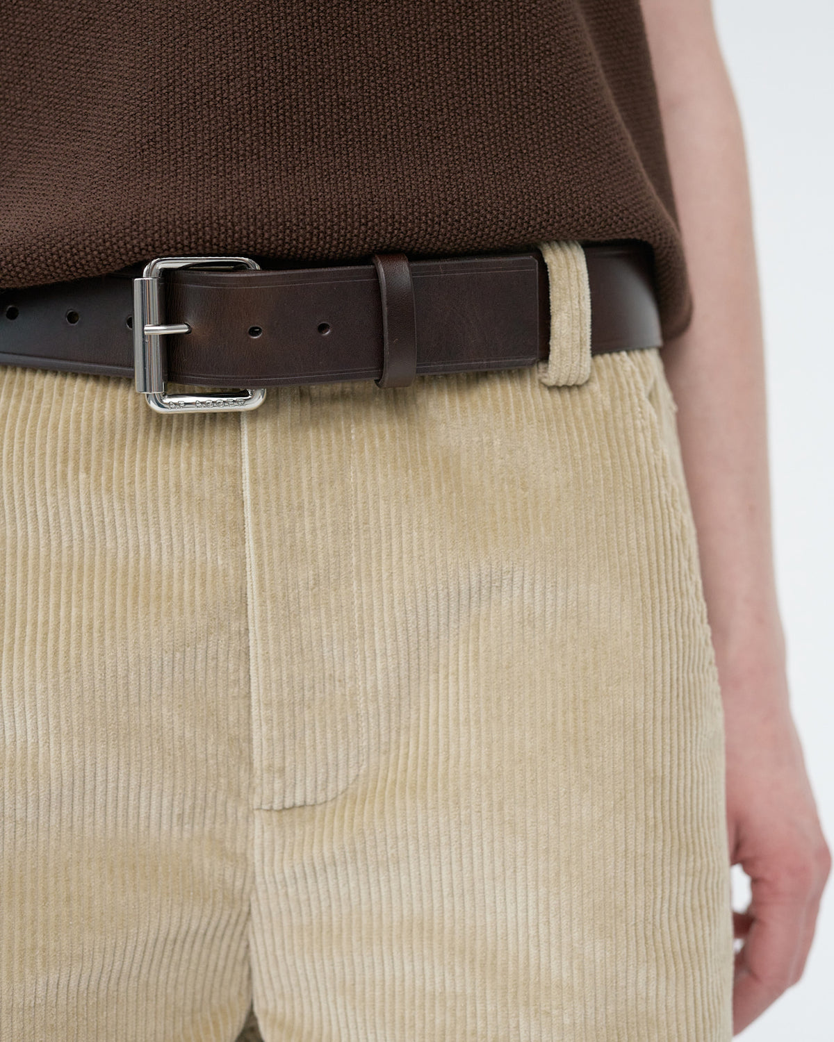 Person wearing a brown belt and beige corduroy pants on a white background
