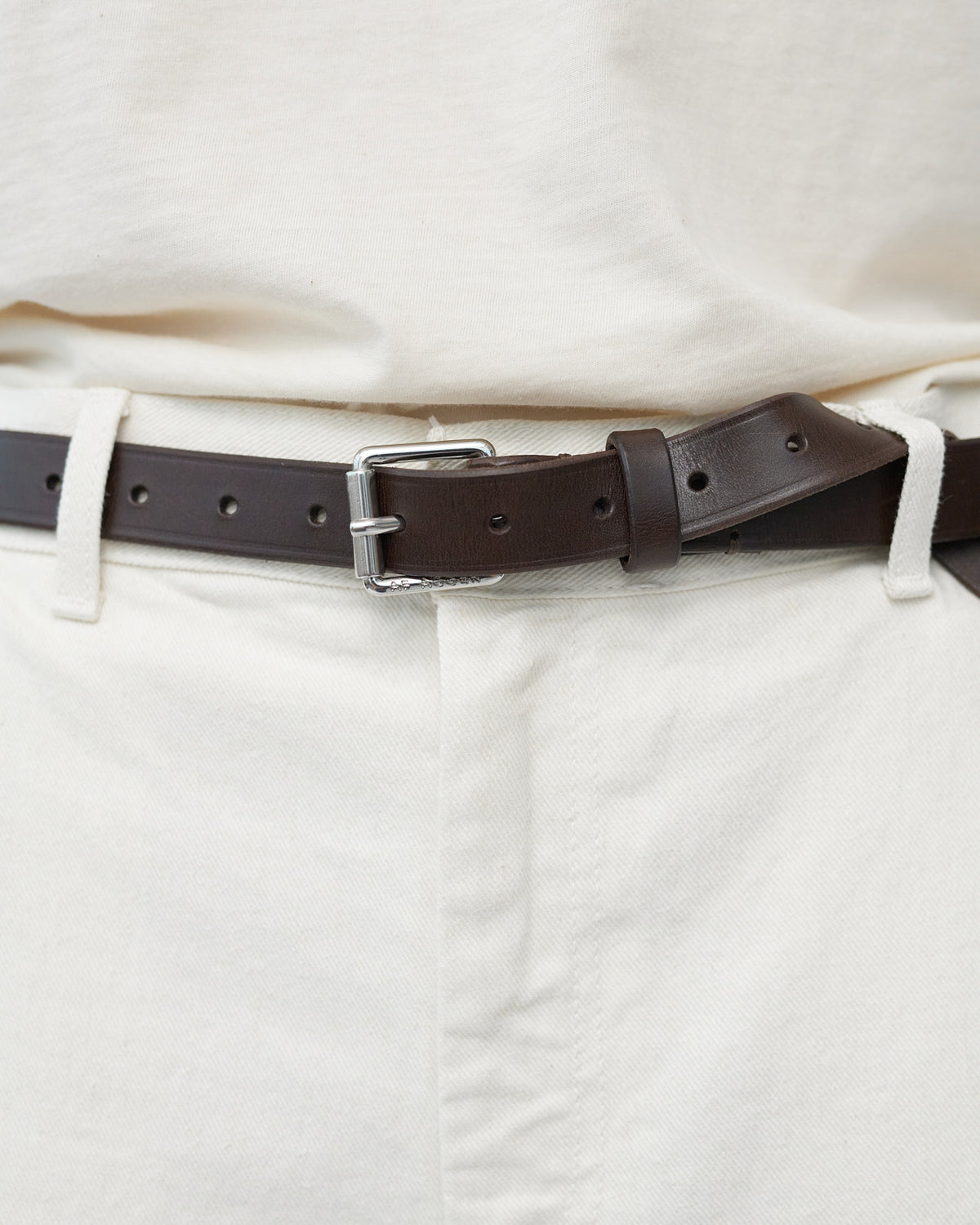 Brown belt with a silver buckle on white pants 