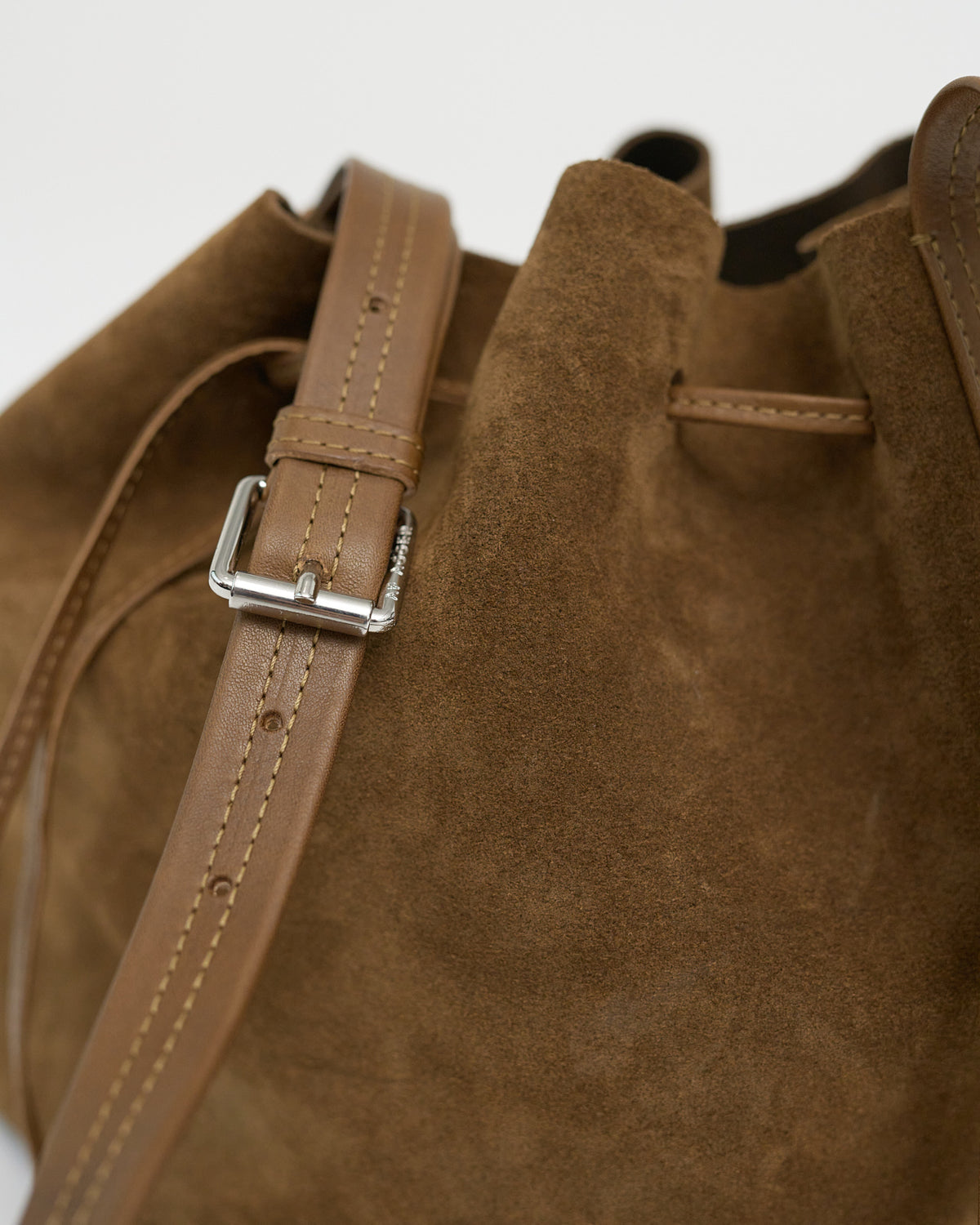 Close-up of a brown leather bag with a strap and buckle on a white background