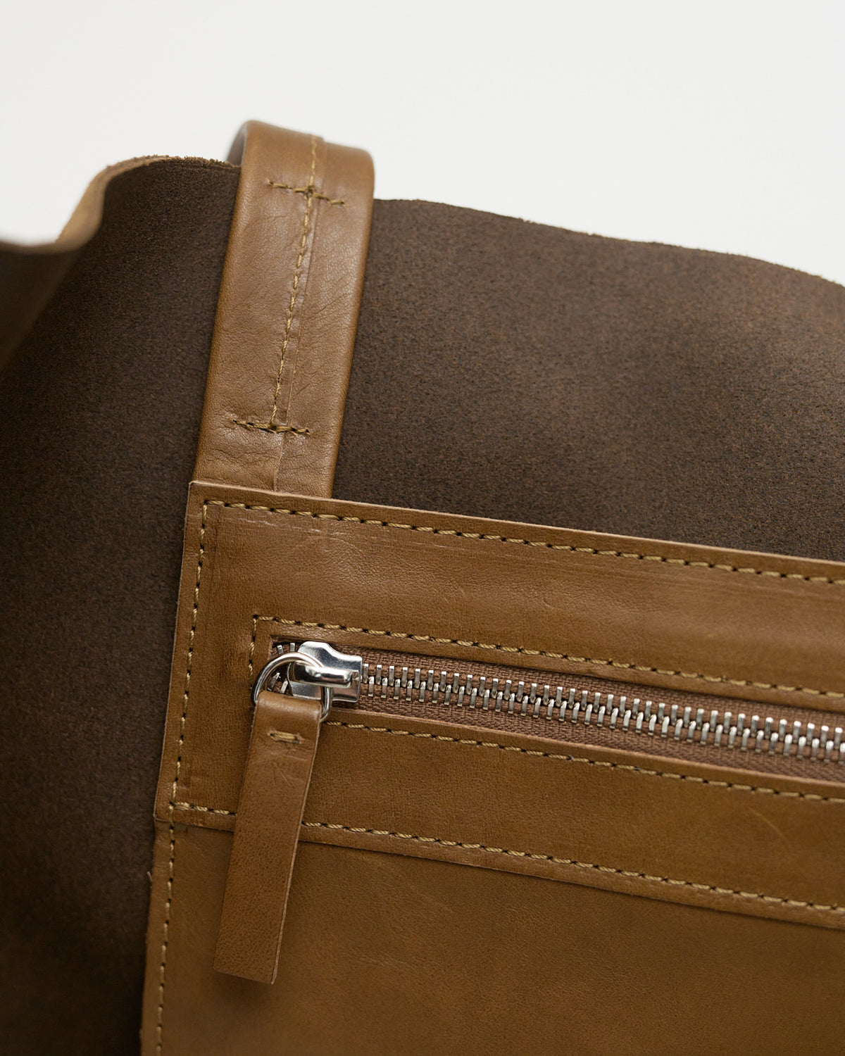 Close-up of a brown leather bag with a zipper on a light gray background